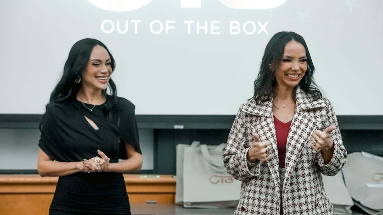 Duas profissionais do OTB diante do painel Out of the Box em auditório acadêmico em Boston.
